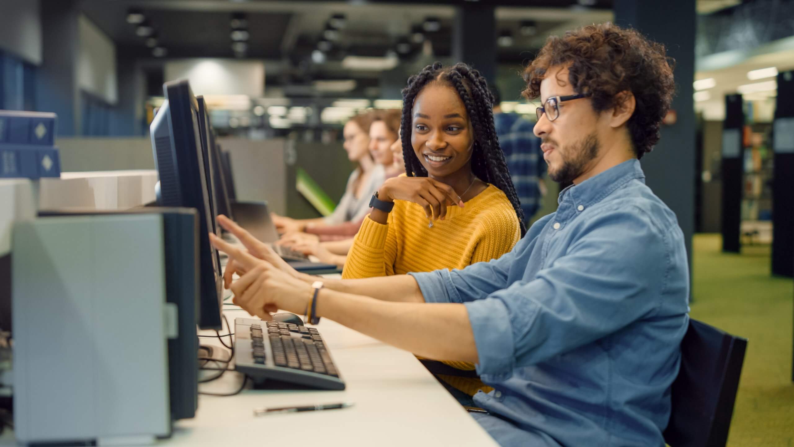 University Library: Bright Black Girl and Smart Hispanic Boy Together Work on Computers, Chat, Discuss Class Assignment, Explain and Advice Each Other. Diverse Group of Students Exam Study Teamwork